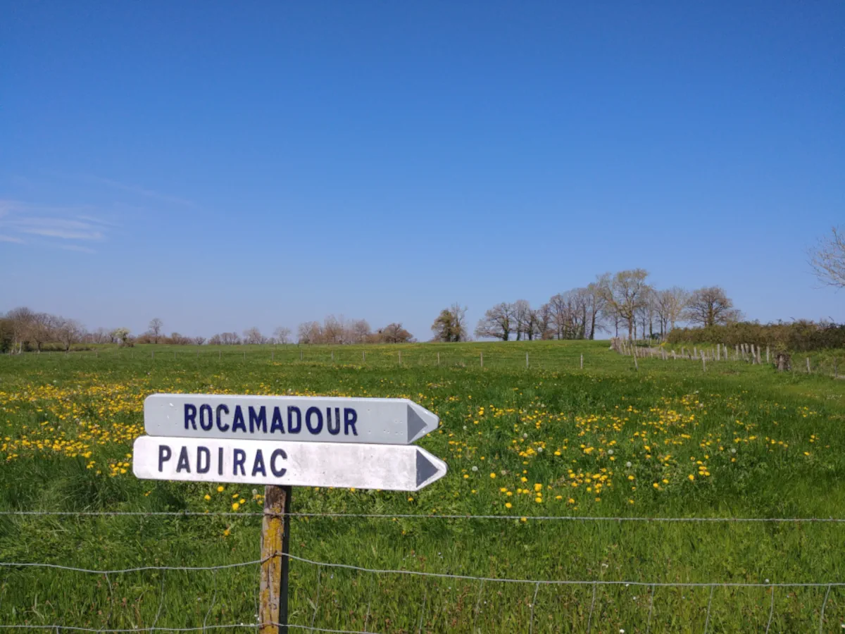 Panneaux de signalisation routiĂšre indiquant Rocamadour et le Gouffre de Padirac devant une prairie fleurie dans le Lot.